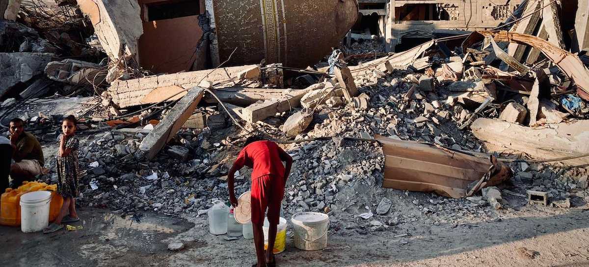 Una persona coge agua entre las ruinas ,mientras Gaza declara la emergencia sanitaria. | Foto: UNRWA