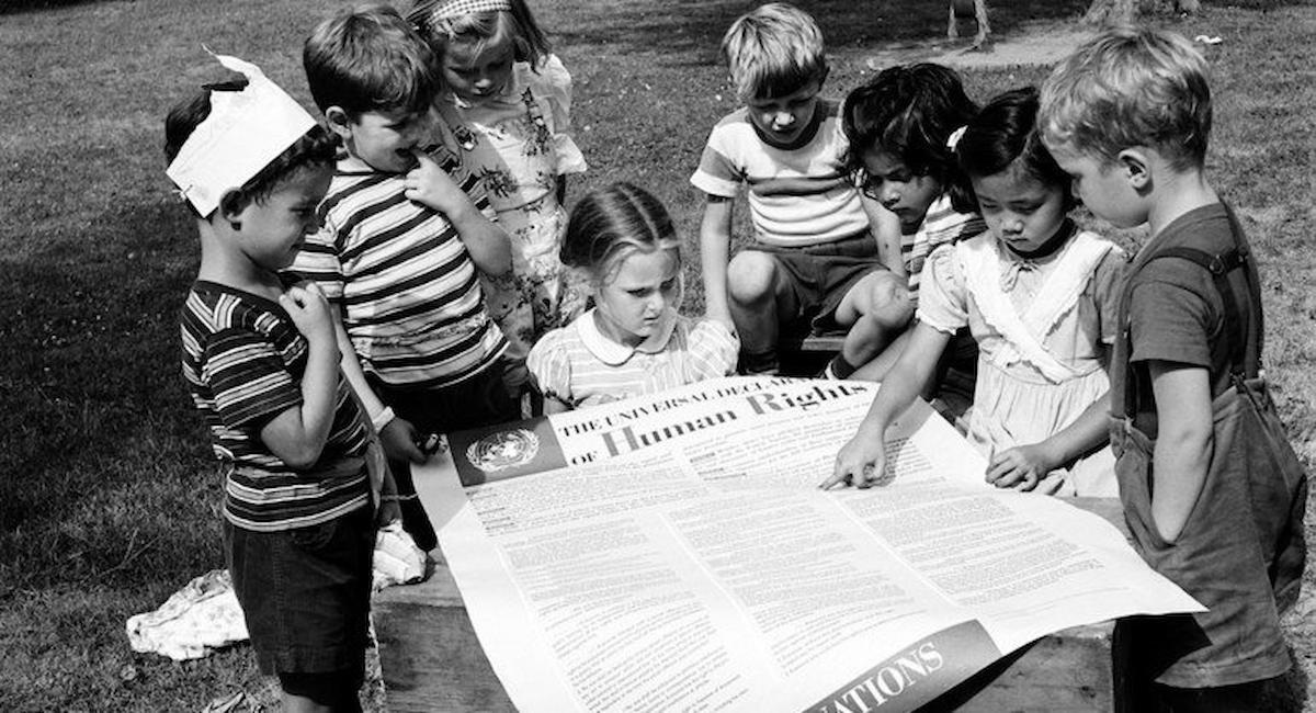 Valor Multilateralismo - Un grupo de niñas y niños leen la Declaración Universal de Derechos Humanos, un documento de gran valor datado en 1948. | Foto: ONU