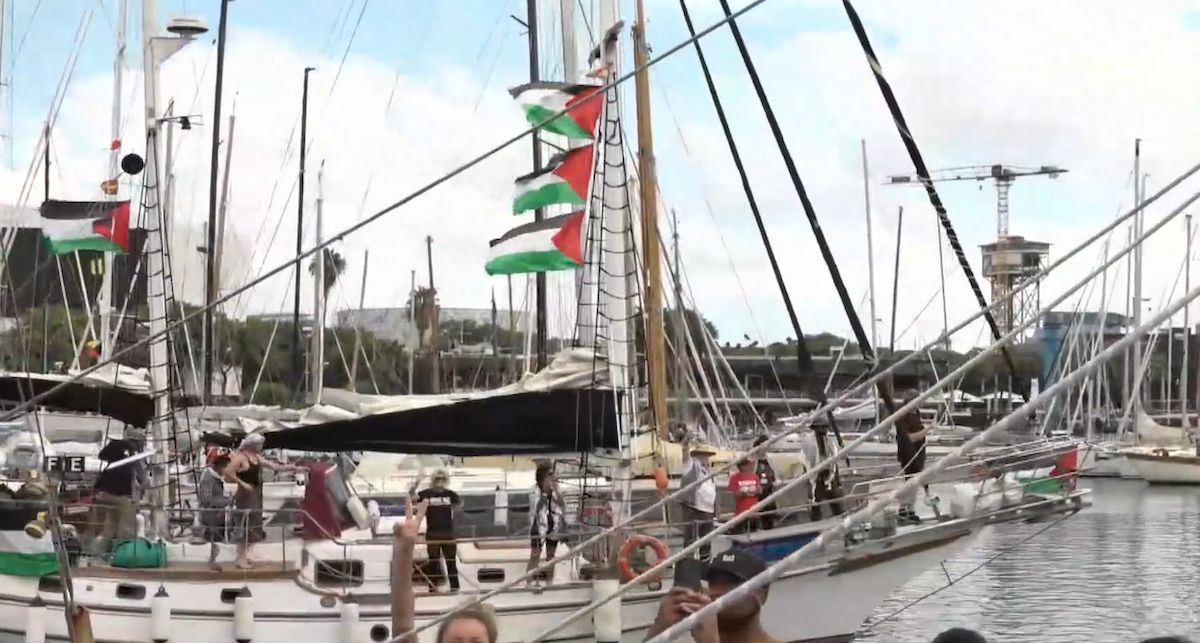 Una de las embarcaciones de la Global Sumud Flotilla y algunos activistas saludando al salir del puerto de Barcelona.