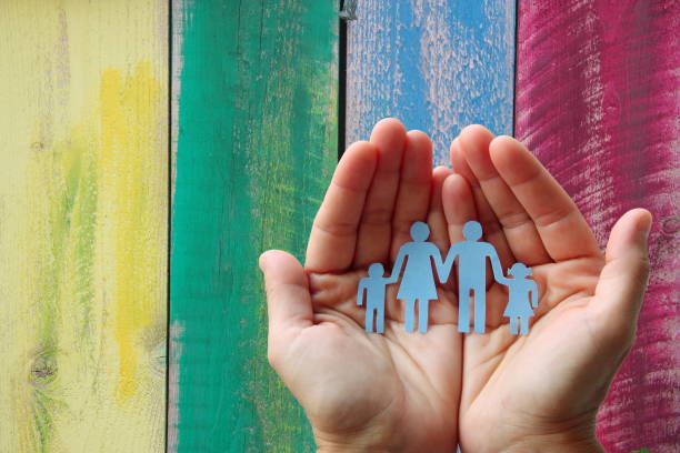 Paper family in hands on wooden coloured background welfare concept