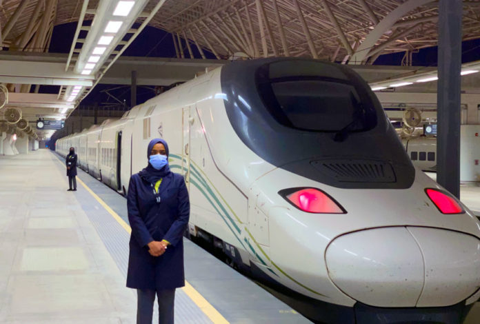 Trabajadora Saudí de Renfe posando con uno de los trenes de la compañía de fondo.